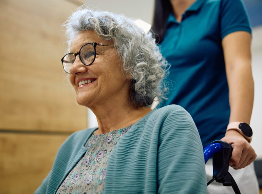 An elderly woman in an assisted living facility getting assistance from a caregiver.