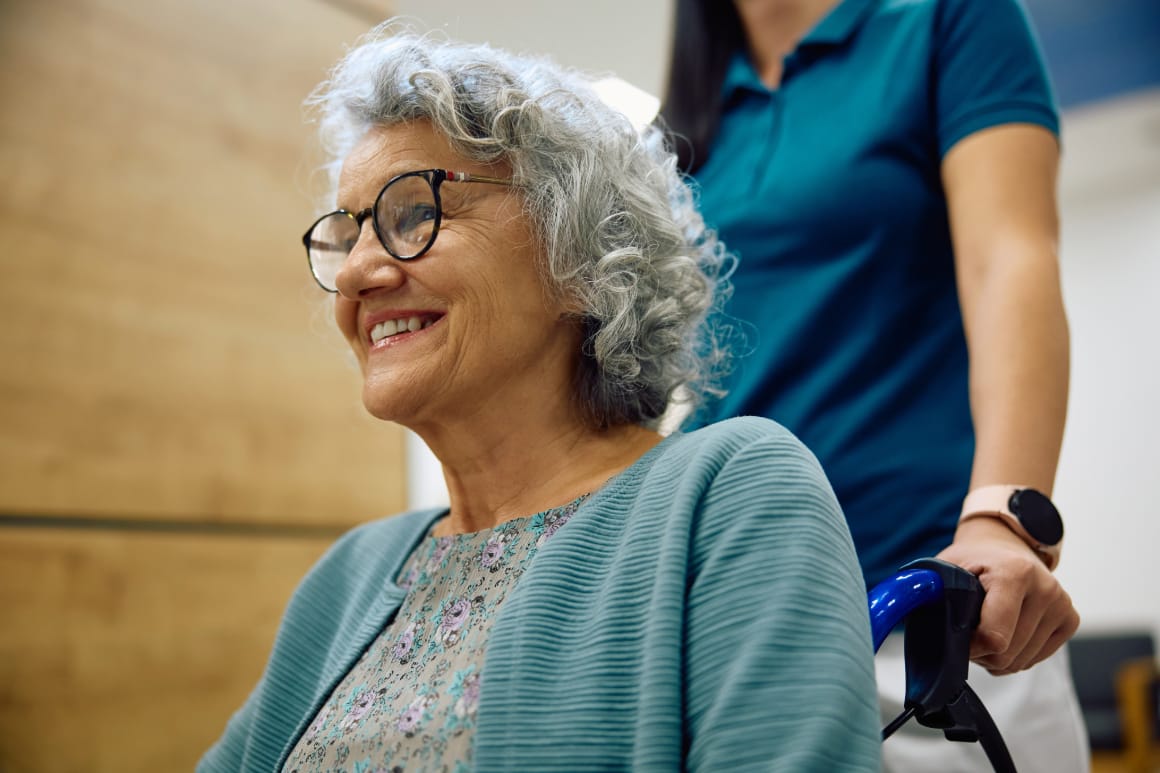 An elderly woman in an assisted living facility getting assistance from a caregiver.