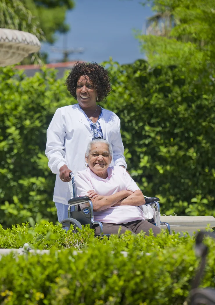 A caregiver pushing a smiling resident in a wheelchair through the St. Margaret's courtyard garden