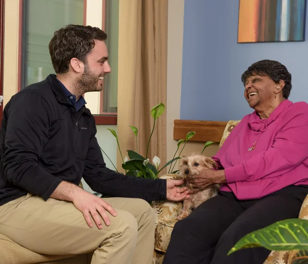A St. Margaret's staff member laughing with a resident and her small dog